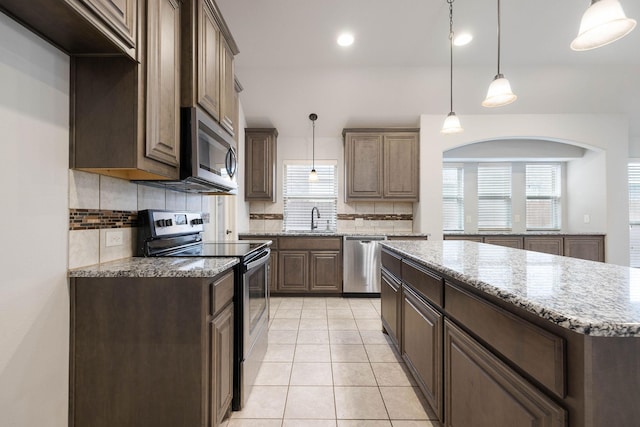 kitchen with sink, light stone counters, a center island, hanging light fixtures, and appliances with stainless steel finishes