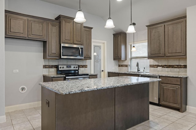 kitchen featuring appliances with stainless steel finishes, sink, hanging light fixtures, a center island, and light stone countertops