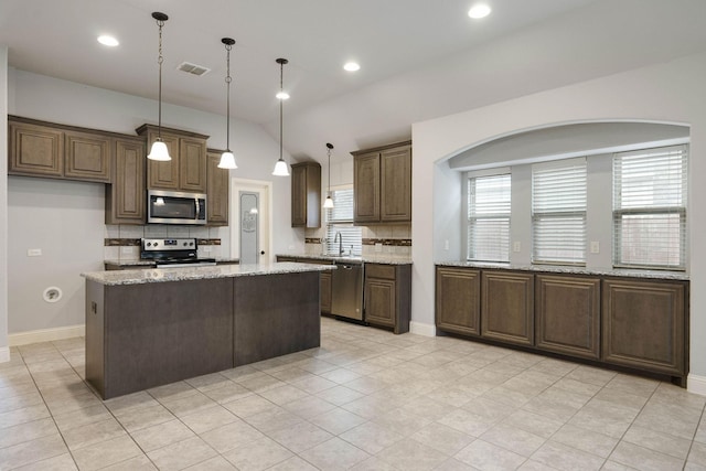 kitchen with hanging light fixtures, stainless steel appliances, a center island, light stone counters, and tasteful backsplash