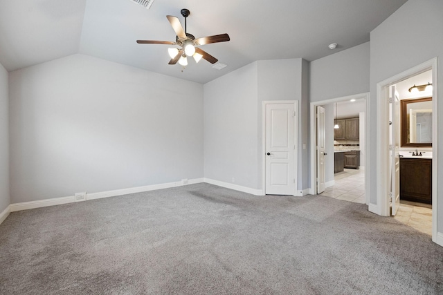 unfurnished bedroom with connected bathroom, a sink, light colored carpet, baseboards, and vaulted ceiling