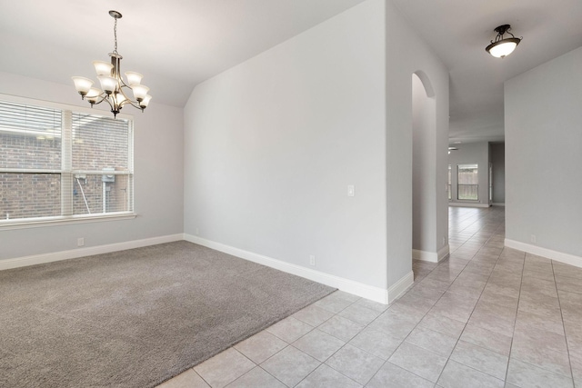 empty room with light tile patterned floors, arched walkways, a notable chandelier, and a wealth of natural light