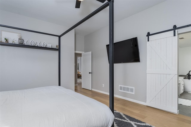 bedroom with a barn door, hardwood / wood-style floors, and ceiling fan