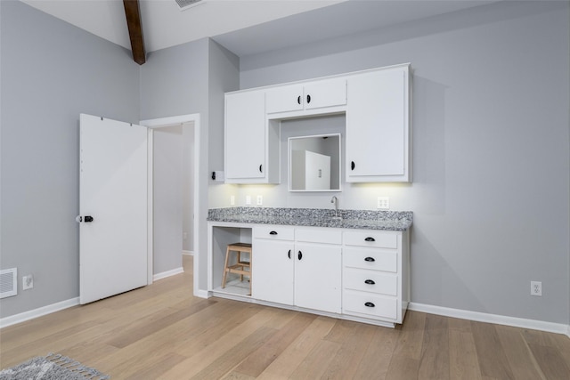 kitchen featuring sink, white cabinets, light stone countertops, beam ceiling, and light hardwood / wood-style flooring