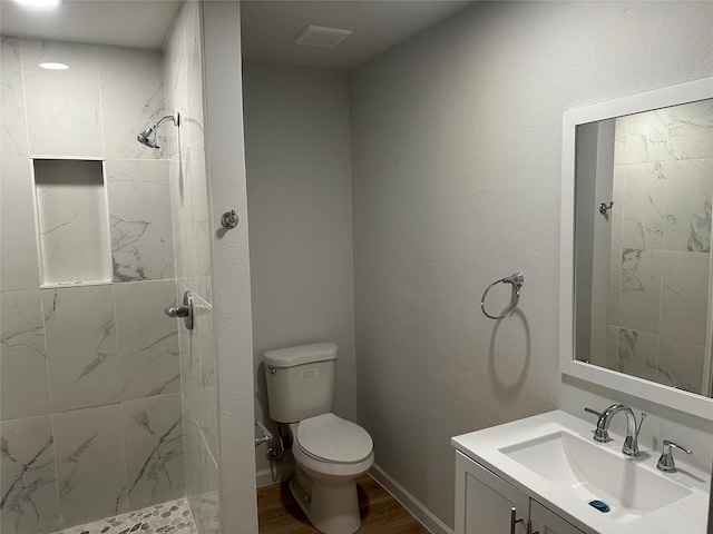 full bath featuring toilet, wood finished floors, a tile shower, baseboards, and vanity