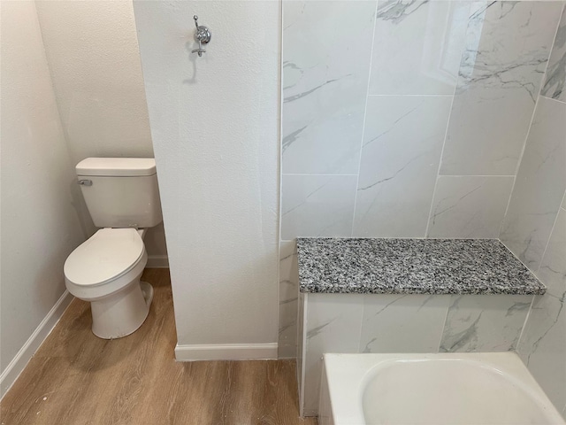 full bathroom with baseboards, toilet, wood finished floors, and a washtub