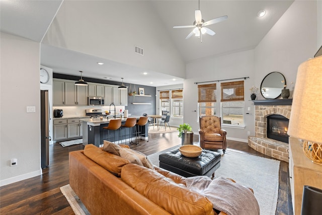 living room with sink, a stone fireplace, high vaulted ceiling, and dark hardwood / wood-style floors