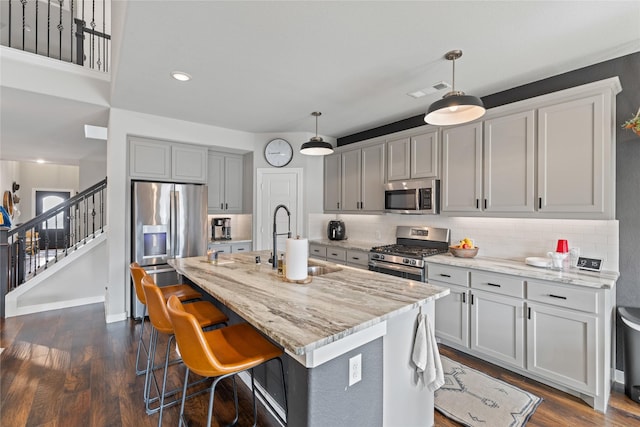 kitchen featuring sink, decorative light fixtures, appliances with stainless steel finishes, light stone countertops, and a kitchen island with sink