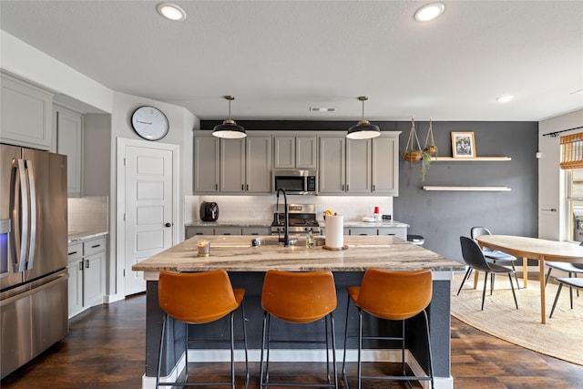 kitchen featuring gray cabinetry, decorative light fixtures, dark hardwood / wood-style flooring, stainless steel appliances, and a kitchen island with sink