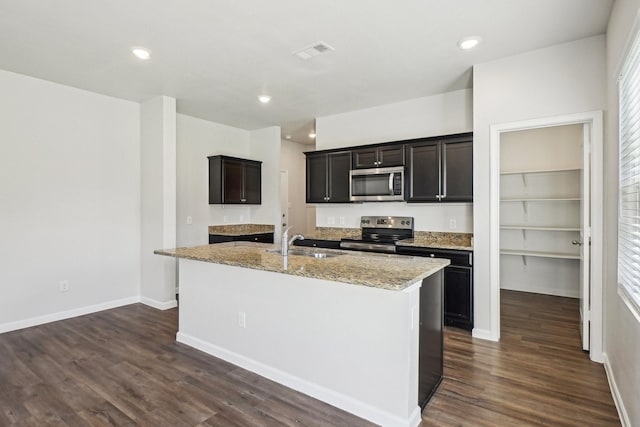 kitchen with sink, light stone counters, stainless steel appliances, dark wood-type flooring, and a center island with sink