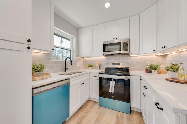 kitchen with sink, light wood-type flooring, white cabinets, and appliances with stainless steel finishes