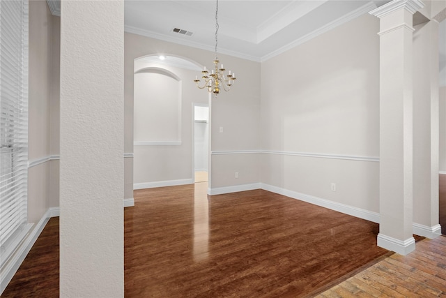 unfurnished dining area with ornate columns, crown molding, an inviting chandelier, a tray ceiling, and dark hardwood / wood-style flooring