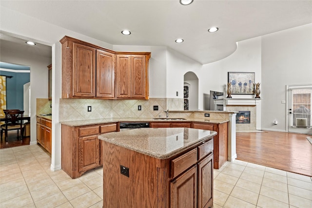 kitchen featuring light tile patterned floors, sink, a tile fireplace, light stone counters, and a kitchen island