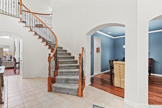 stairs featuring tile patterned flooring, ornamental molding, and a high ceiling