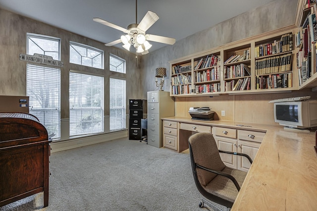 office space featuring built in desk, light colored carpet, and ceiling fan