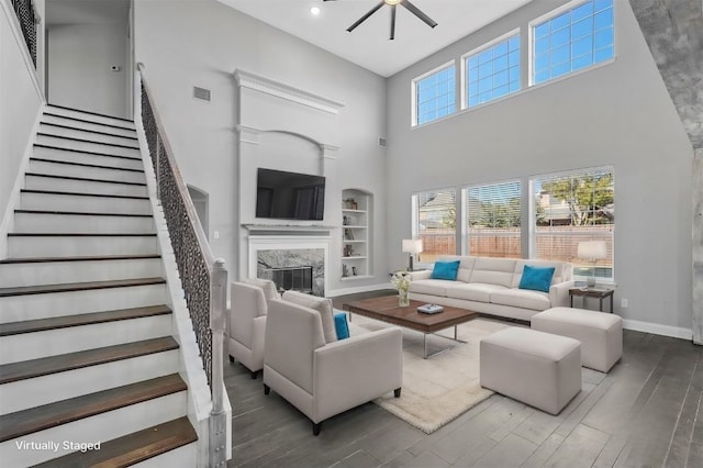 living room featuring a premium fireplace, ceiling fan, a high ceiling, dark hardwood / wood-style flooring, and built in shelves