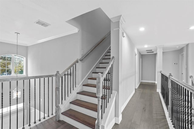 staircase featuring crown molding, wood-type flooring, a chandelier, and ornate columns