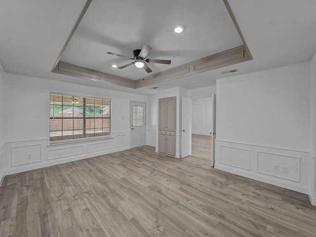 spare room with ceiling fan, a tray ceiling, and light wood-type flooring