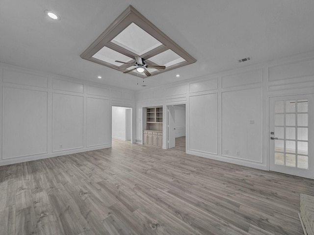 unfurnished living room with crown molding, ceiling fan, a skylight, and light hardwood / wood-style flooring