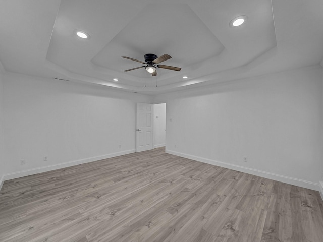 unfurnished room with a raised ceiling, ceiling fan, and light hardwood / wood-style floors