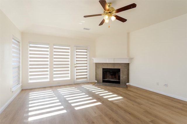 unfurnished living room featuring a tiled fireplace, ceiling fan, light hardwood / wood-style flooring, and a healthy amount of sunlight