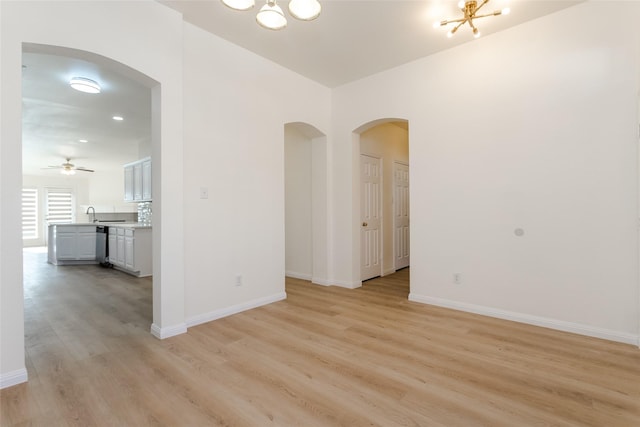 spare room featuring ceiling fan with notable chandelier and light hardwood / wood-style flooring