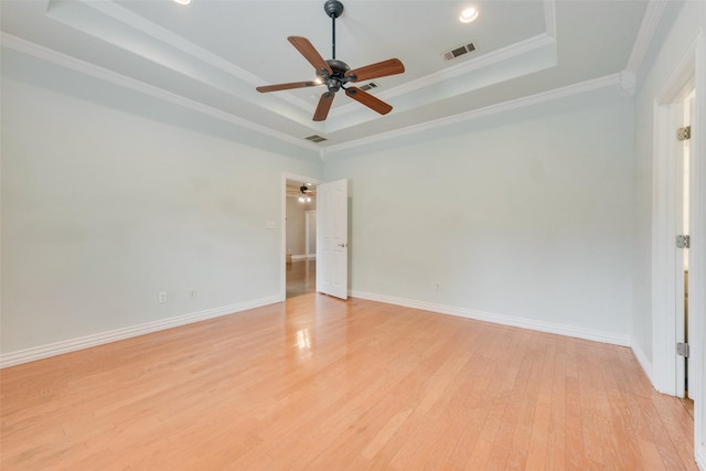 empty room with a raised ceiling, ornamental molding, ceiling fan, and light hardwood / wood-style floors