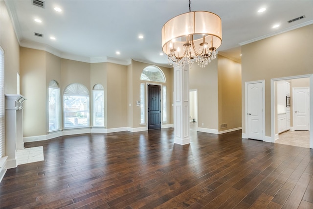 unfurnished living room featuring dark wood-type flooring, ornate columns, a chandelier, ornamental molding, and a towering ceiling