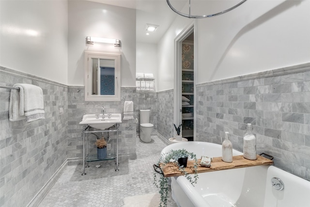 bathroom with toilet, sink, tile walls, a tub, and tile patterned flooring