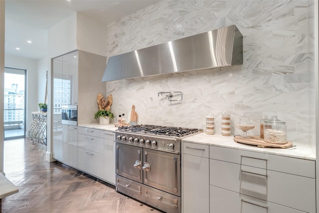 kitchen with backsplash, wall chimney exhaust hood, light stone countertops, parquet floors, and stainless steel gas stovetop