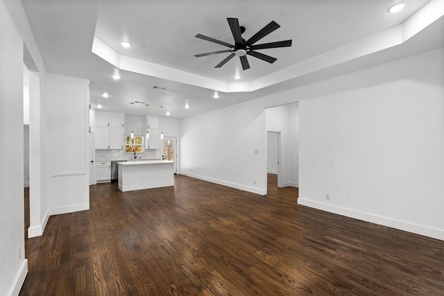 unfurnished living room featuring dark wood-type flooring, ceiling fan, a raised ceiling, and sink