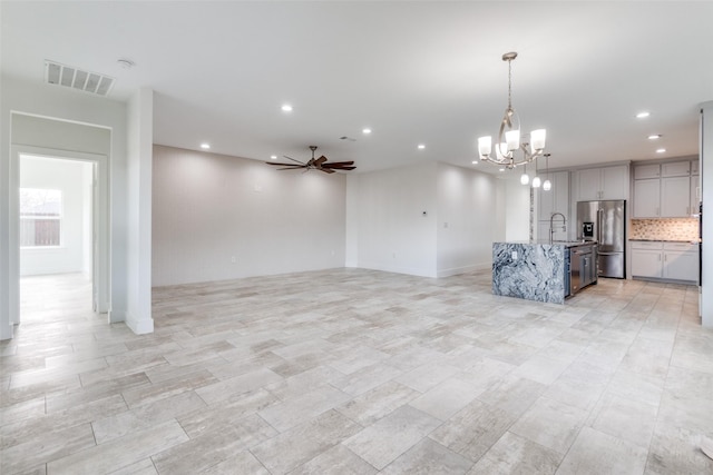 unfurnished living room with recessed lighting, visible vents, a sink, and ceiling fan with notable chandelier