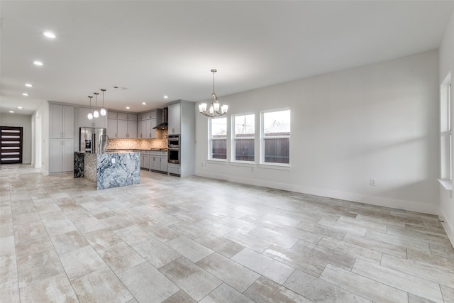 kitchen featuring gray cabinetry, appliances with stainless steel finishes, open floor plan, wall chimney range hood, and a chandelier