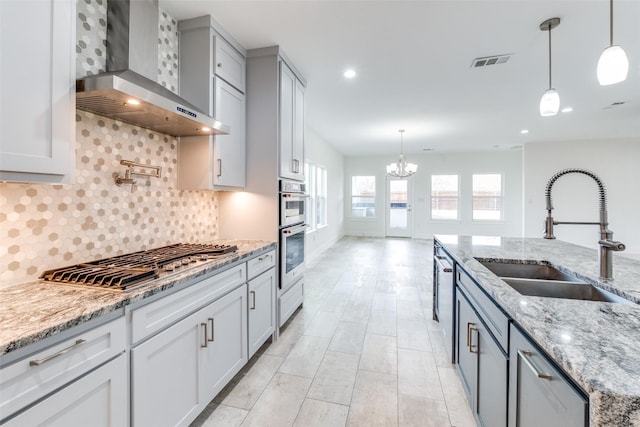 kitchen with stainless steel appliances, visible vents, a sink, light stone countertops, and wall chimney exhaust hood