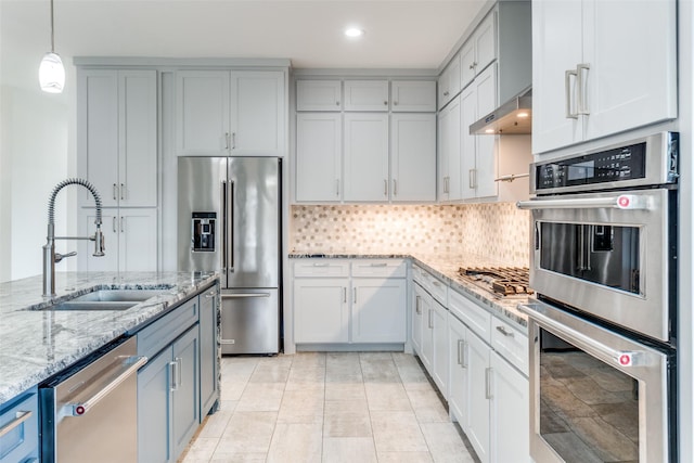 kitchen with decorative backsplash, appliances with stainless steel finishes, light stone counters, under cabinet range hood, and a sink