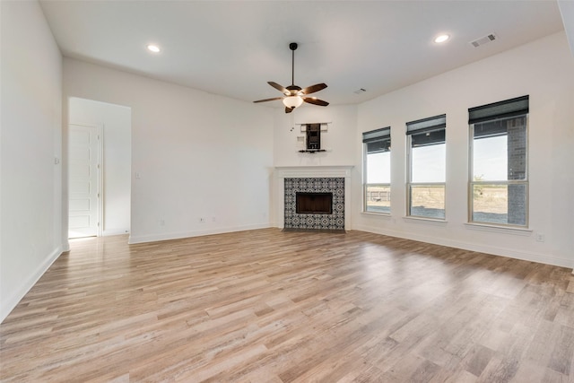 unfurnished living room featuring a tiled fireplace, light hardwood / wood-style flooring, and ceiling fan