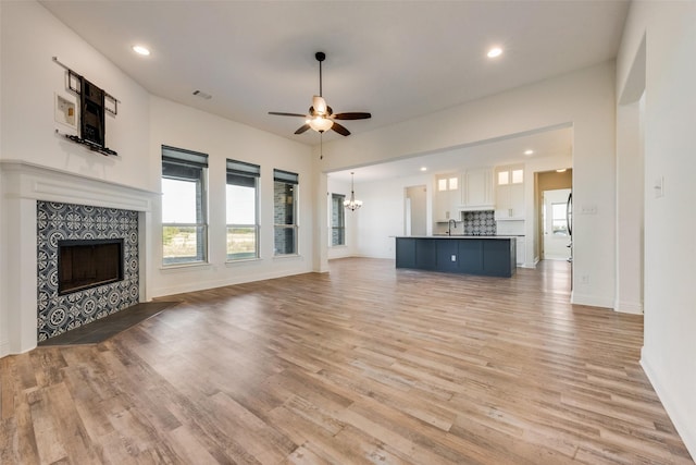 unfurnished living room featuring sink, ceiling fan with notable chandelier, a tile fireplace, and light wood-type flooring