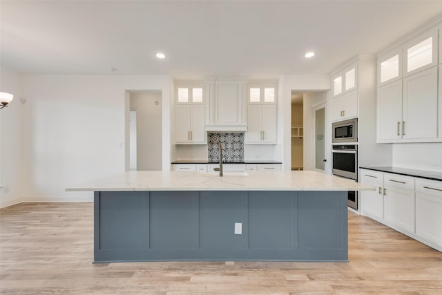 kitchen with light stone counters, white cabinets, a large island with sink, and appliances with stainless steel finishes