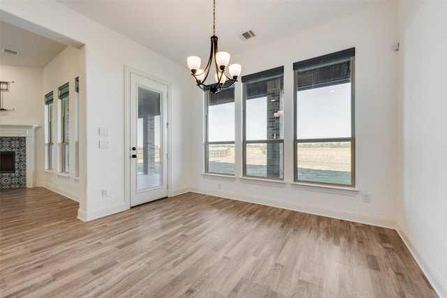 unfurnished dining area featuring a fireplace, a chandelier, and light hardwood / wood-style floors