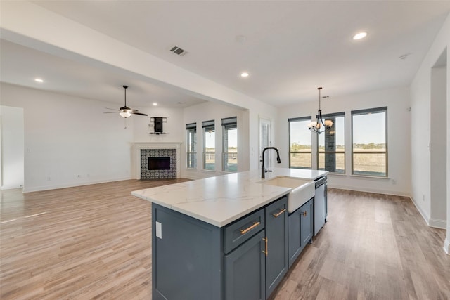 kitchen with a wealth of natural light, a fireplace, hanging light fixtures, light stone countertops, and a center island with sink