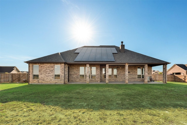 rear view of property featuring a patio, a yard, and solar panels