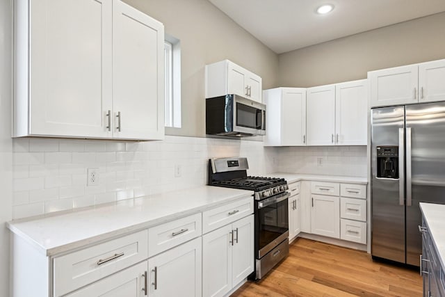 kitchen featuring appliances with stainless steel finishes, white cabinetry, backsplash, light stone counters, and light hardwood / wood-style floors