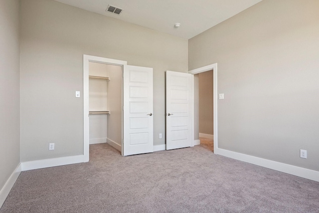 unfurnished bedroom with a walk in closet, a closet, and light carpet