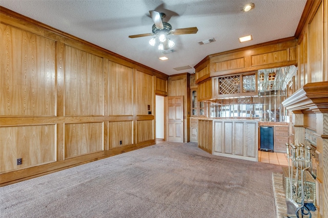 unfurnished living room with ceiling fan, wooden walls, light carpet, and a textured ceiling