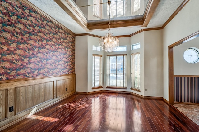 unfurnished room featuring an inviting chandelier, wood-type flooring, a textured ceiling, ornamental molding, and a raised ceiling