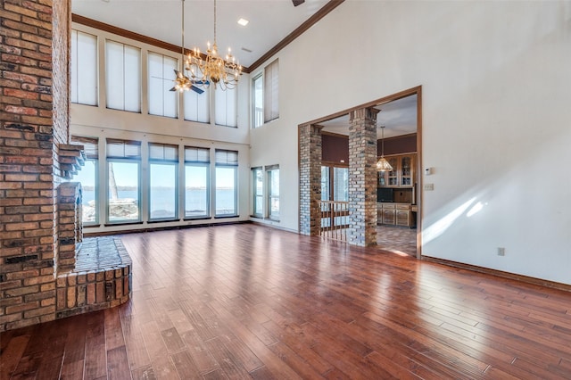 unfurnished living room featuring ornate columns, hardwood / wood-style floors, a chandelier, a high ceiling, and crown molding