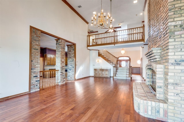 unfurnished living room featuring crown molding, hardwood / wood-style flooring, a towering ceiling, a brick fireplace, and a chandelier