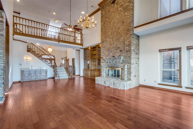 unfurnished living room featuring ceiling fan with notable chandelier, a brick fireplace, a towering ceiling, and hardwood / wood-style floors