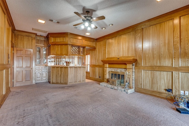 unfurnished living room with wood walls, ornamental molding, ceiling fan, light carpet, and a textured ceiling