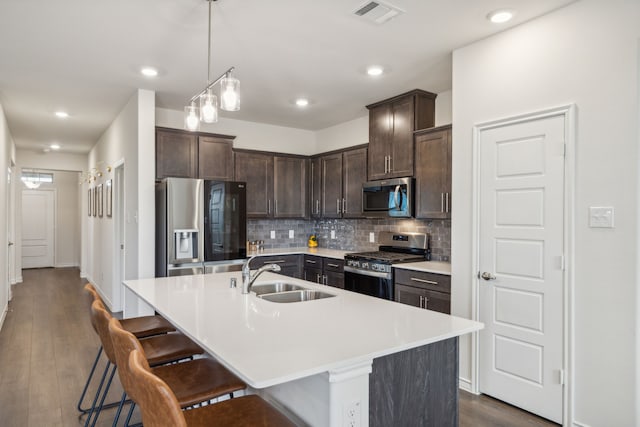 kitchen with sink, tasteful backsplash, dark brown cabinets, stainless steel appliances, and a kitchen island with sink