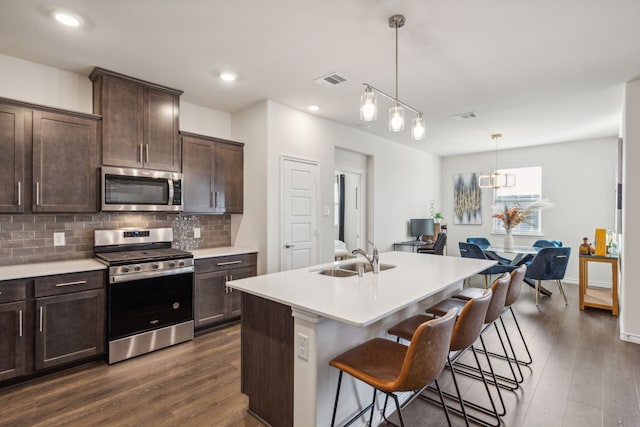 kitchen featuring sink, a breakfast bar, a kitchen island with sink, stainless steel appliances, and decorative light fixtures